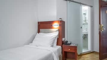 Een hotelkamer met een bed, nachtkastje en een schuifdeur naar de badkamer.