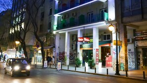 A multi-story building with balconies, a ground-floor shop, and a visible sign for 'Tatios'.