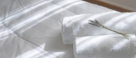 Un lit bien fait, avec du linge de lit blanc et une petite branche de lavande posée sur le dessus.