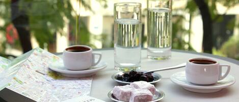 A table with a menu, two cups of coffee, a glass of water, and a plate of Turkish delight.