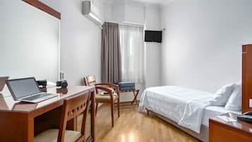 Habitación de hotel con un escritorio de madera, una laptop, una silla, una cama y un televisor montado en la pared.