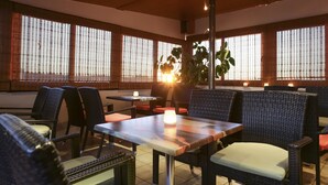 A restaurant with wicker furniture, wooden tables, and large windows with blinds. - Attalos Hotel (Athens)