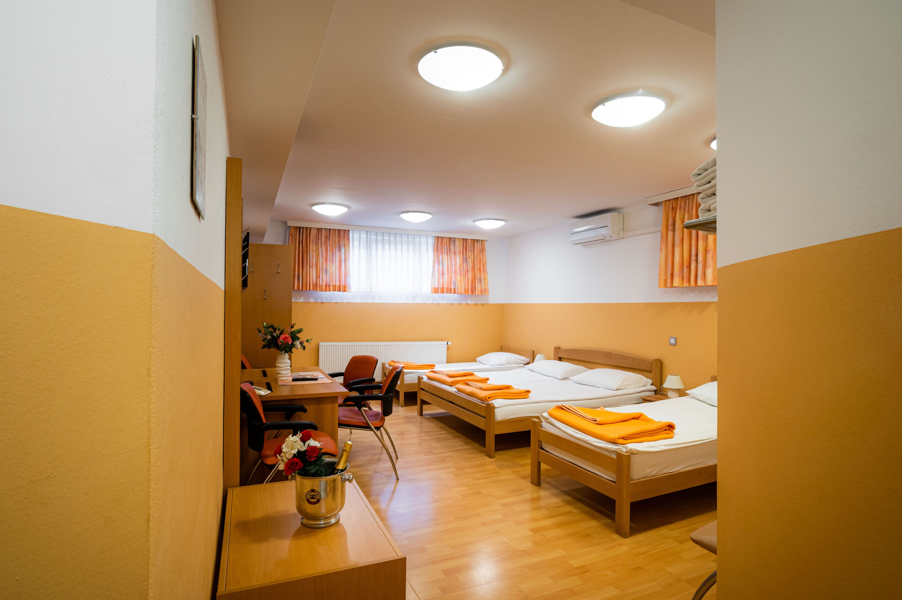 A hotel room with two beds, a desk, a chair, and a small table with flowers.
