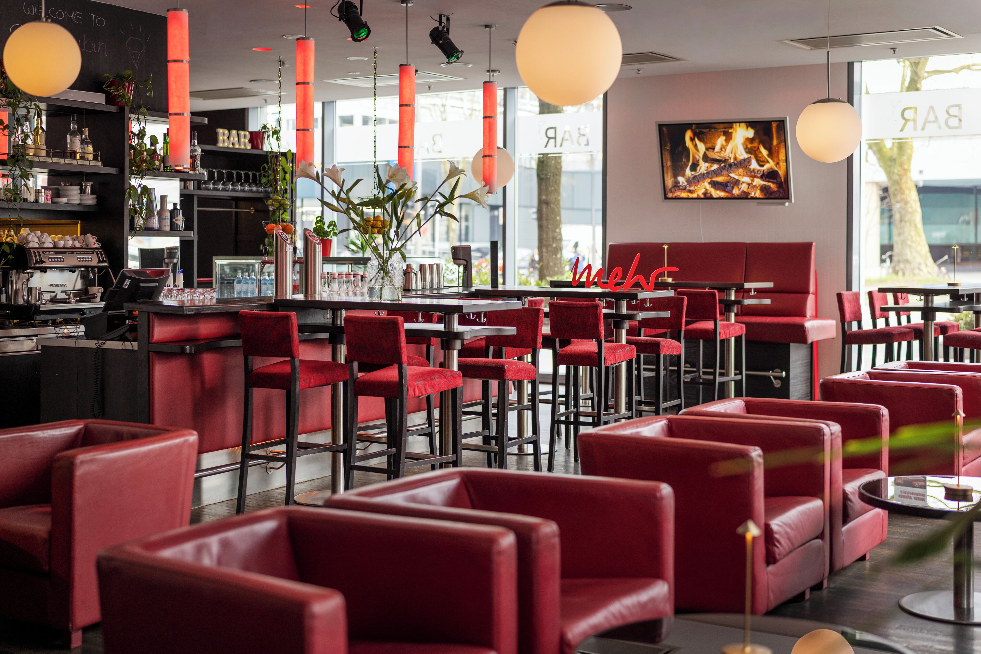 A bar area with red chairs, a bar counter, and a large window with a view.