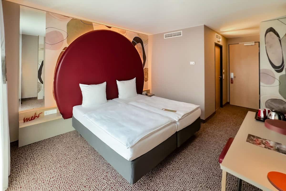 Habitación de hotel con una cama grande, un escritorio, un espejo y una pared de acento roja.