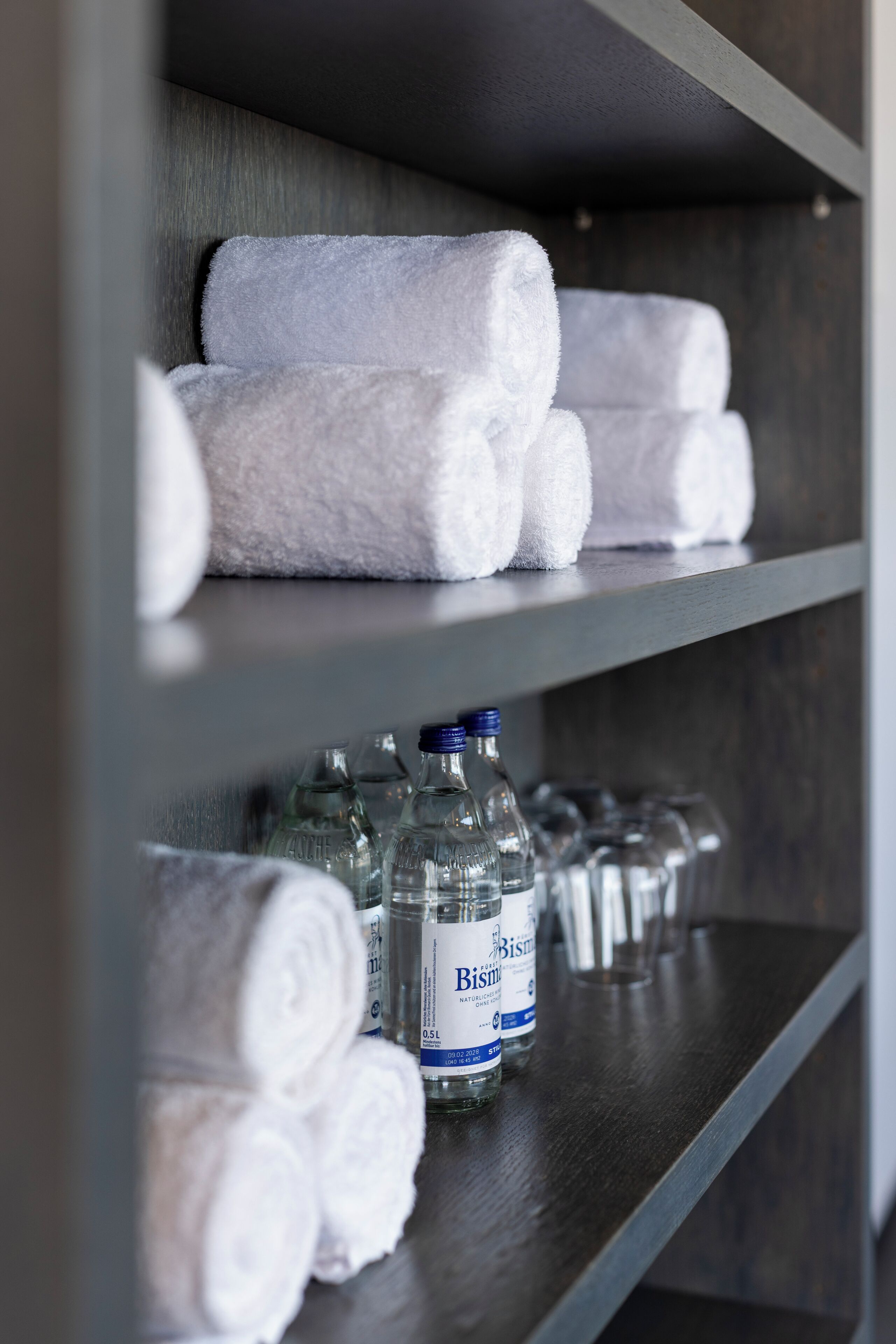 A shelf with white towels and Bismuth water bottles.