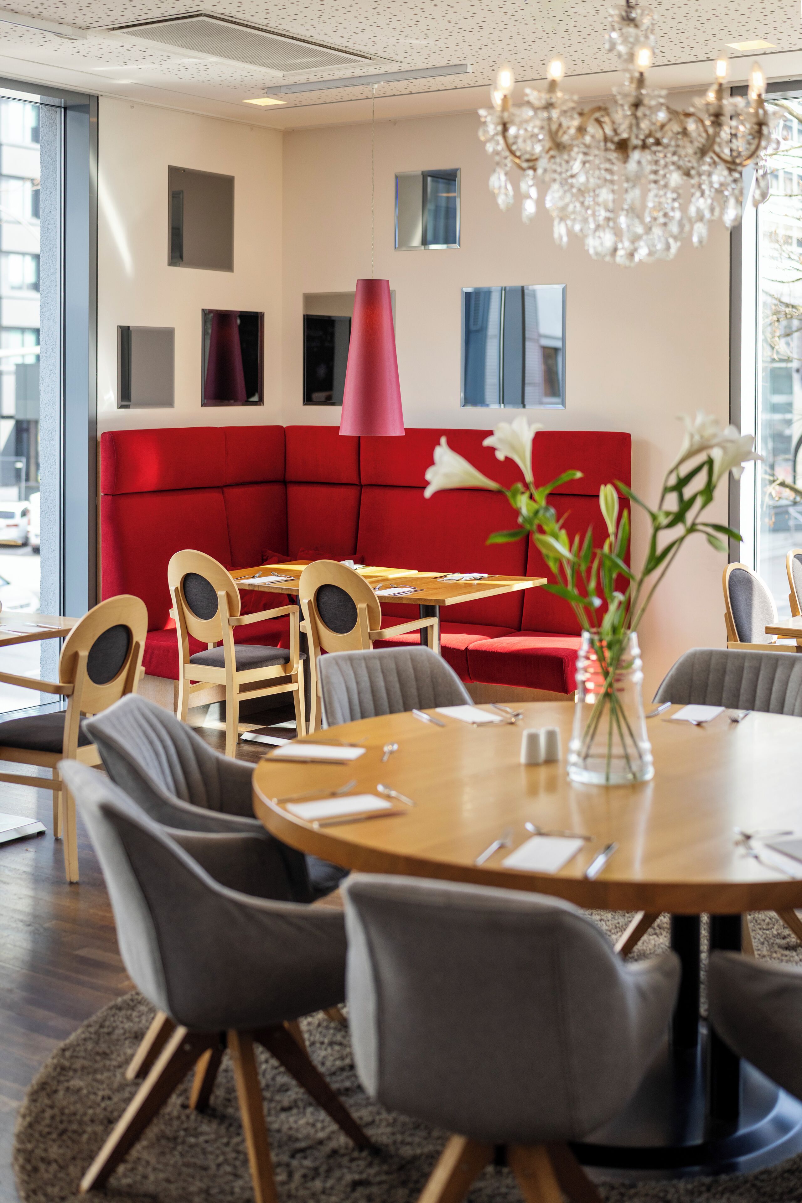 Un espace repas moderne avec une table ronde, des chaises grises, un coin salon rouge et un lustre.