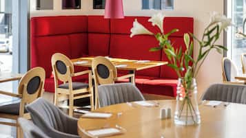 A modern dining area with a round table, grey chairs, a red booth, and a chandelier.