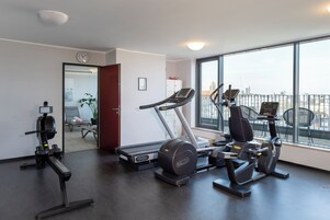 Ein Fitnessstudio mit Laufband, Crosstrainer und Kraftmaschine, großen Fenstern und Blick auf die Stadt.