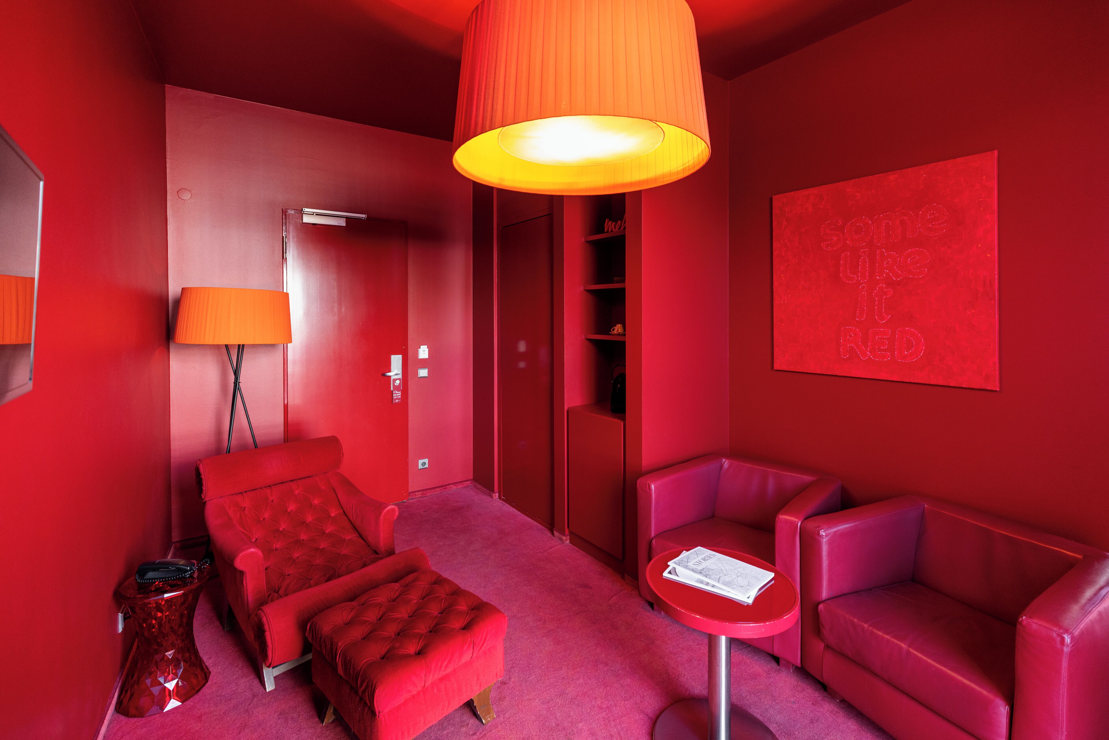Habitación de color rojo con cama, dos sillones, una mesita y una pared roja con un letrero que dice 'some like it RED'.