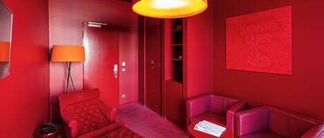 Habitación de color rojo con cama, dos sillones, una mesita y una pared roja con un letrero que dice 'some like it RED'.