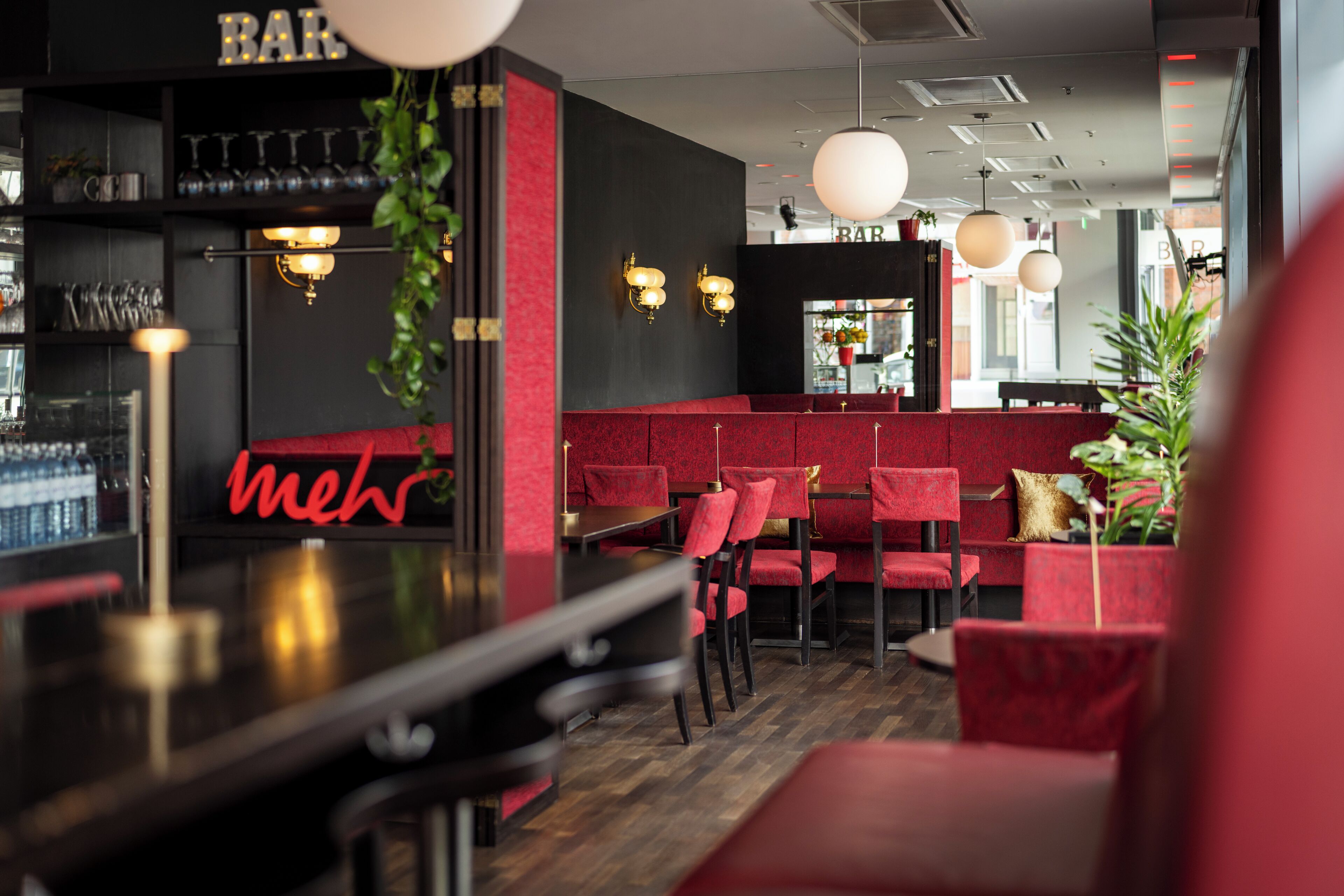 Un área de bar con asientos rojos, un letrero de neón e iluminación colgante.
