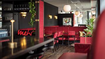 Un área de bar con asientos rojos, un letrero de neón e iluminación colgante.