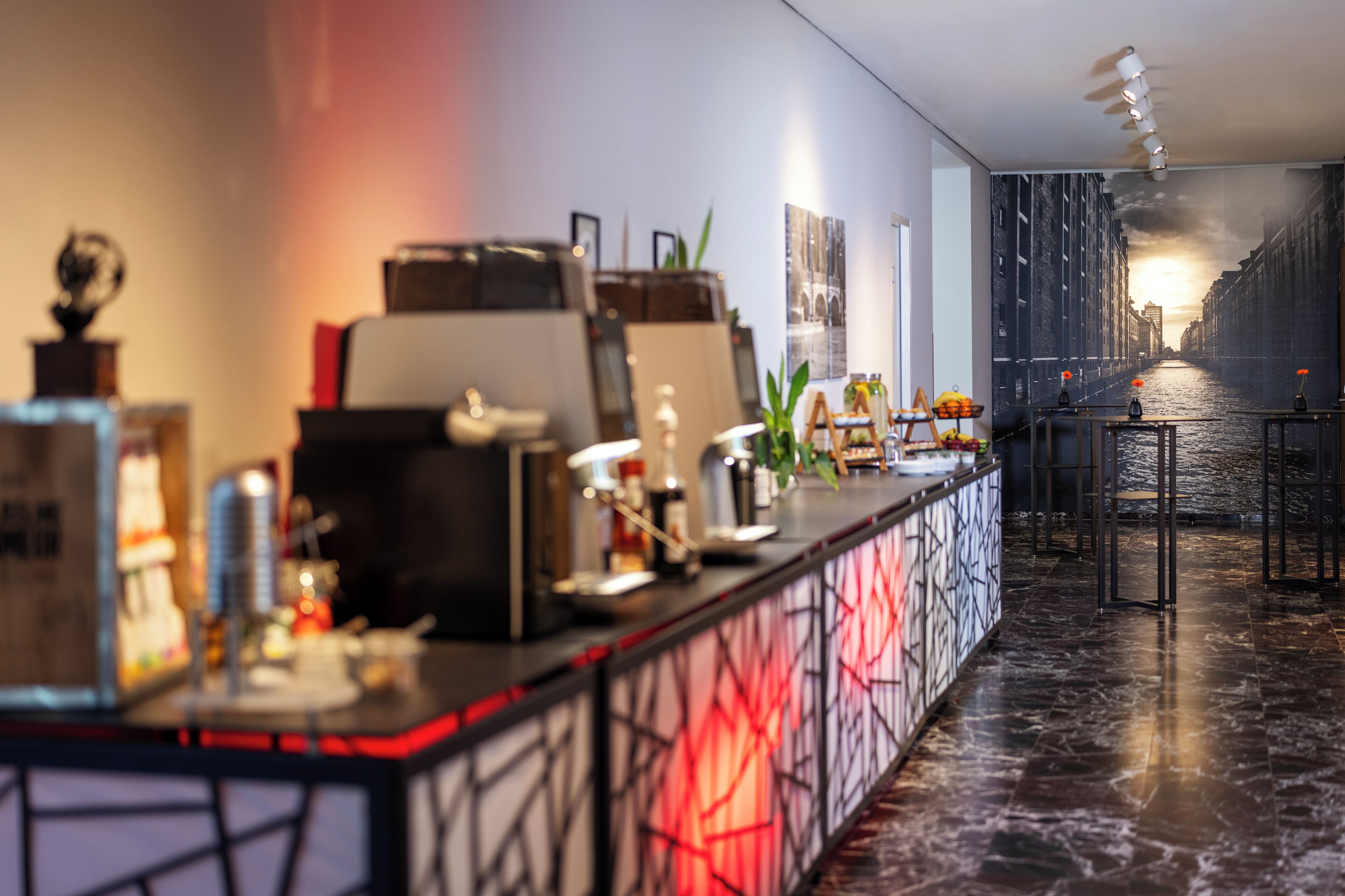 Een moderne hotel lobby met een receptiebalie, een groot muurdecor en uitzicht op een stadsgezicht.