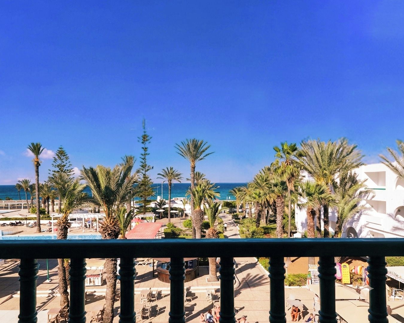 Un complejo turístico frente al mar con palmeras, una piscina y vistas al océano.