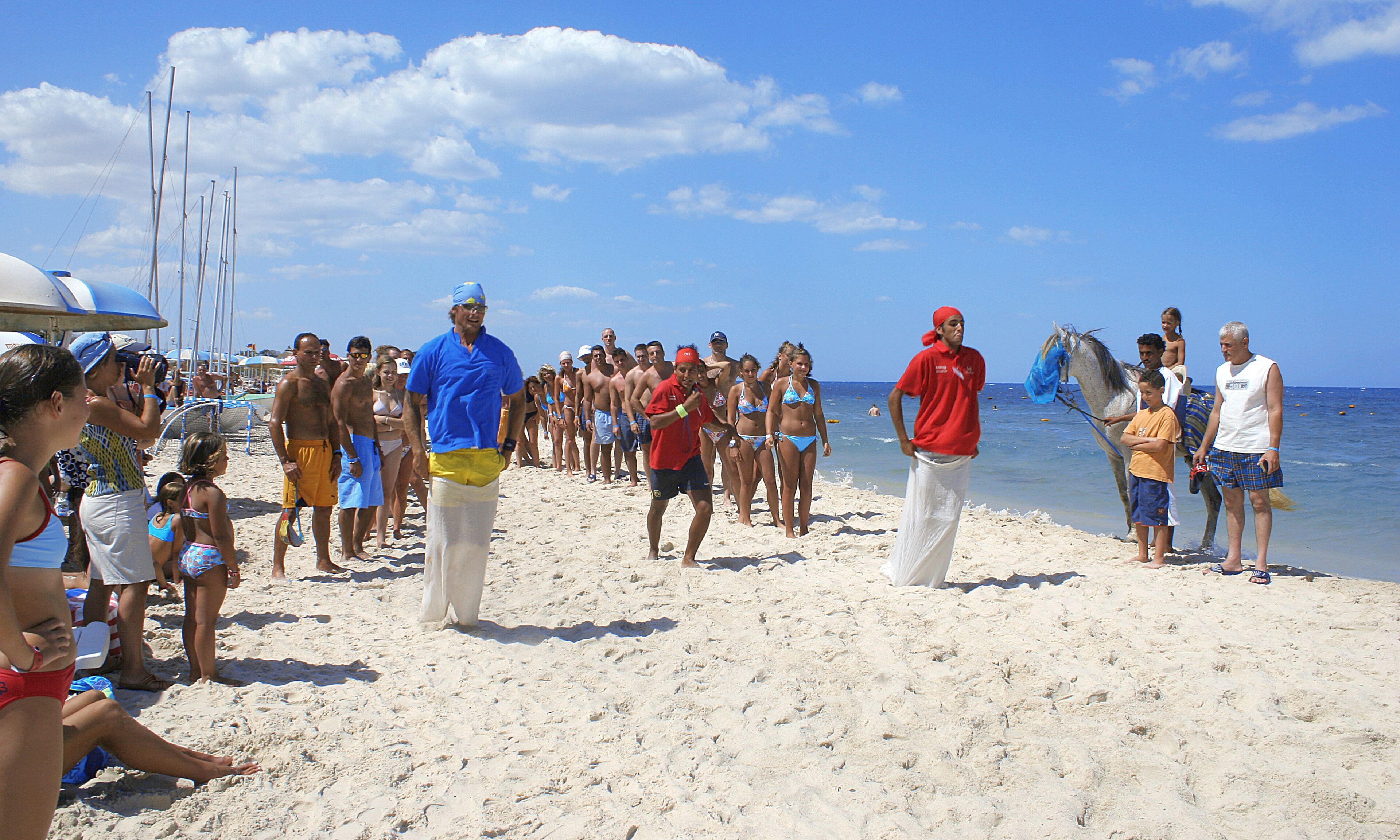 A crowded beach with people and a horse.