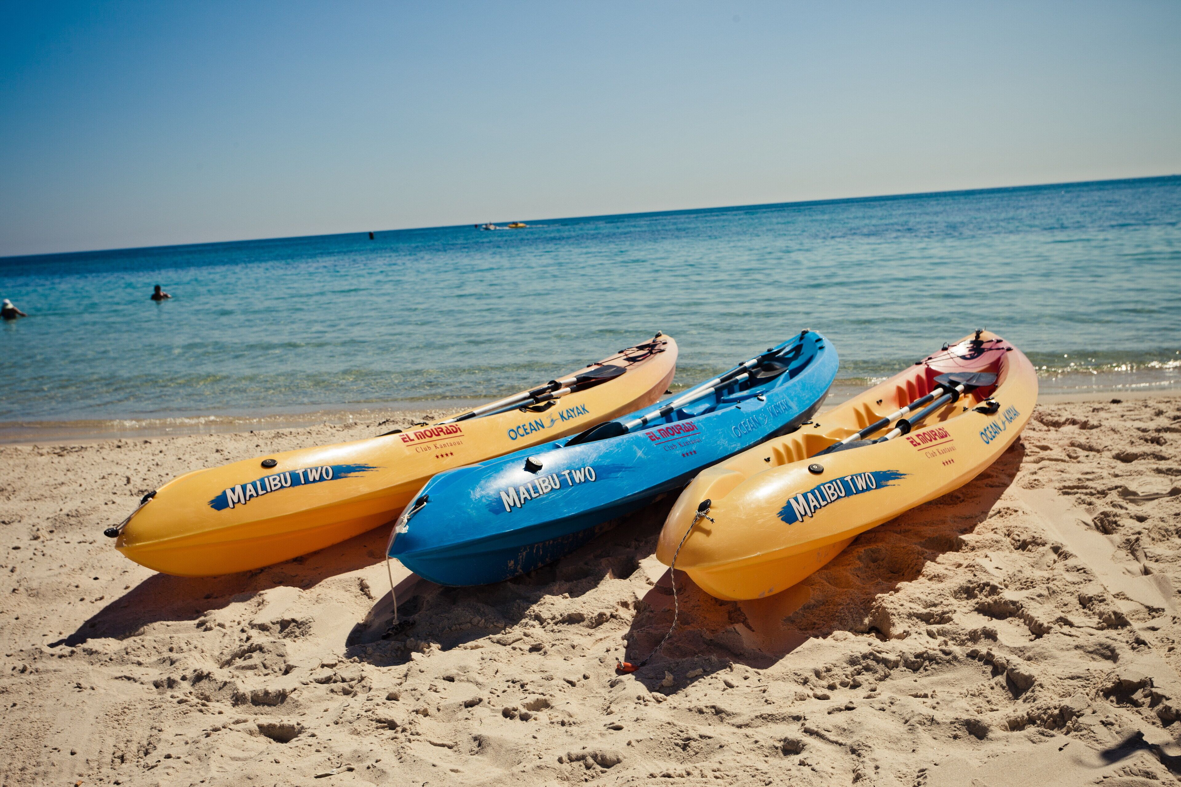 Tre kayak con la scritta 'Malibu Two' su una spiaggia sabbiosa, con l'oceano sullo sfondo.