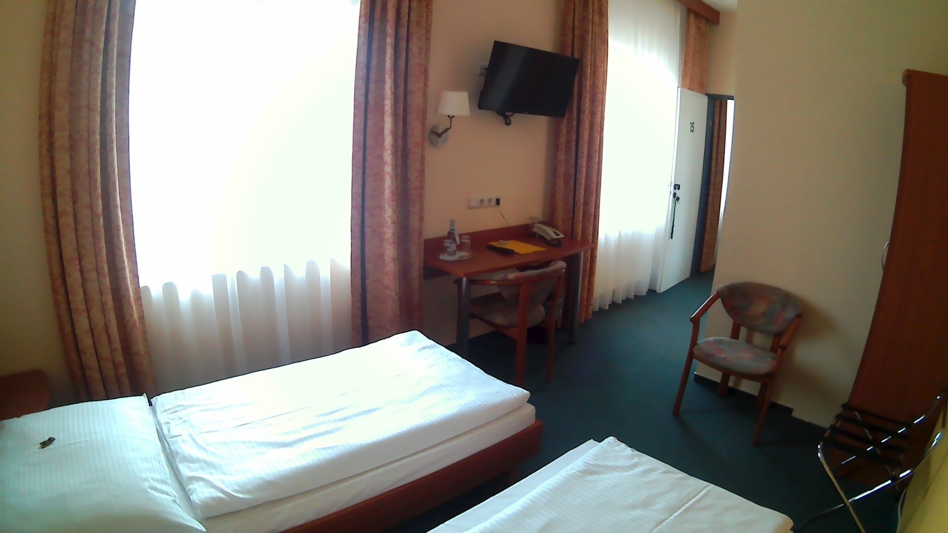 Habitación de hotel con cama, escritorio y silla, televisor en la pared y una puerta.
