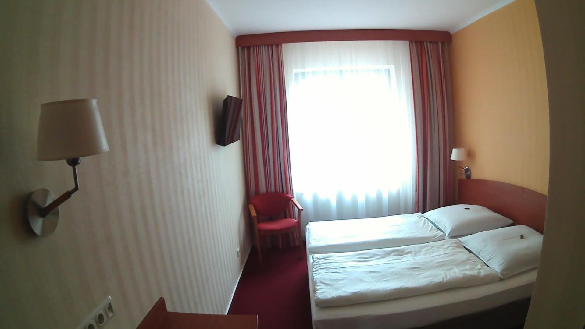 A hotel room with two beds, a TV, a chair, and a window with curtains.