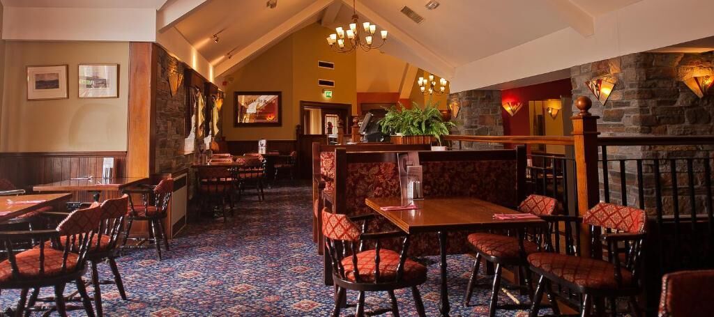 Een restaurant met houten tafels en stoelen, een vloerkleed met patroon, stenen muren en een kroonluchter.