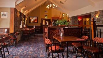 Een restaurant met houten tafels en stoelen, een vloerkleed met patroon, stenen muren en een kroonluchter.