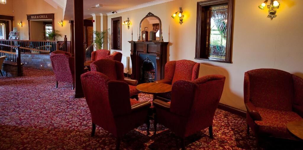 A lobby with red upholstered chairs, a fireplace, and a bar & grill sign.