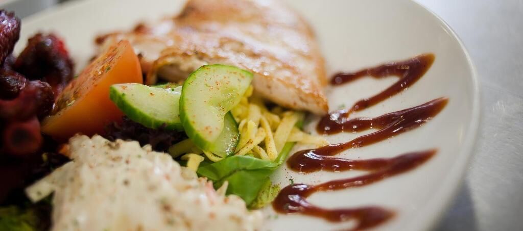 A plate of food with grilled fish, avocado, and a drizzle of sauce.