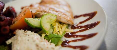 A plate of food with grilled fish, avocado, and a drizzle of sauce.