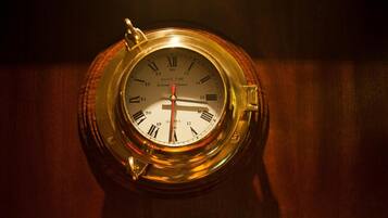 A round, brass ship's clock with Roman numerals and a ship's time indicator.