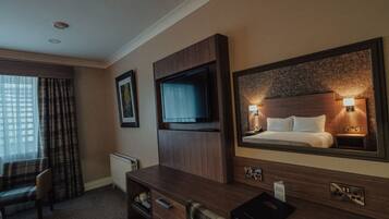 A hotel room with a large bed, a television, a desk with drawers, a chair, and a window with curtains.