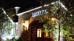 A stone building with a 'HOTEL' sign, a well-lit entrance, and a small porch area. - Corr's Corner Hotel (Newtownabbey)