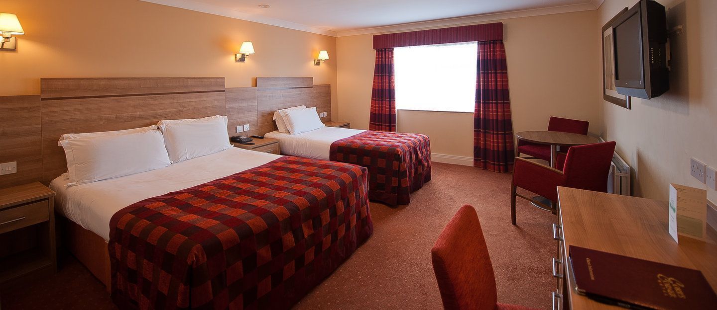 A hotel room with two beds, a desk, a chair, a television, and a window with curtains.