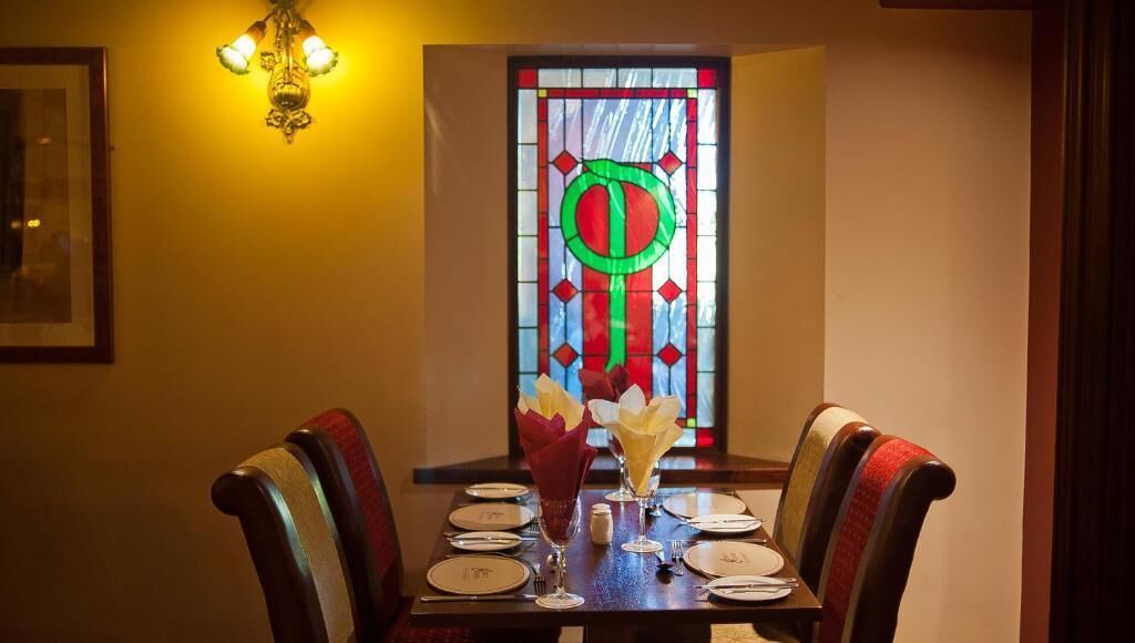 Una mesa para dos, dispuesta con vajilla, con un vitral al fondo.