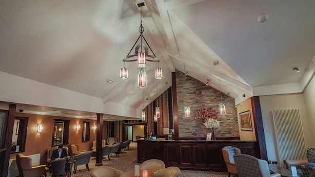 A hotel lobby with a high ceiling, patterned carpet, and a stone accent wall. There are several seating areas with patterned chairs and a reception desk. - Corr's Corner Hotel (Newtownabbey)