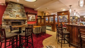 A bar area with a stone fireplace, wooden bar counter, and seating with striped chairs. - Corr's Corner Hotel (Newtownabbey)