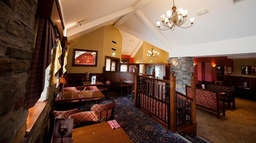 A cozy restaurant with wooden furniture, a stone wall, and a chandelier.