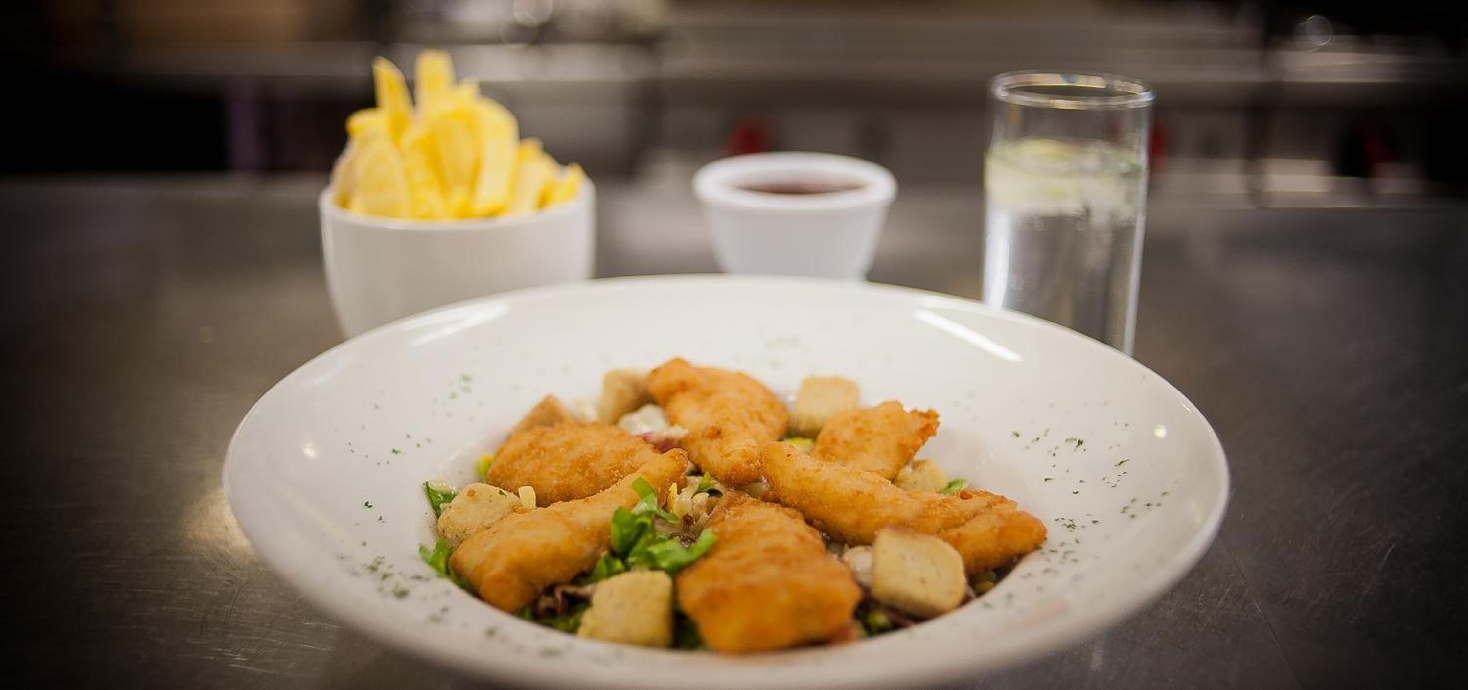 Un plato de comida frita acompañado de papas fritas y un recipiente pequeño con salsa.