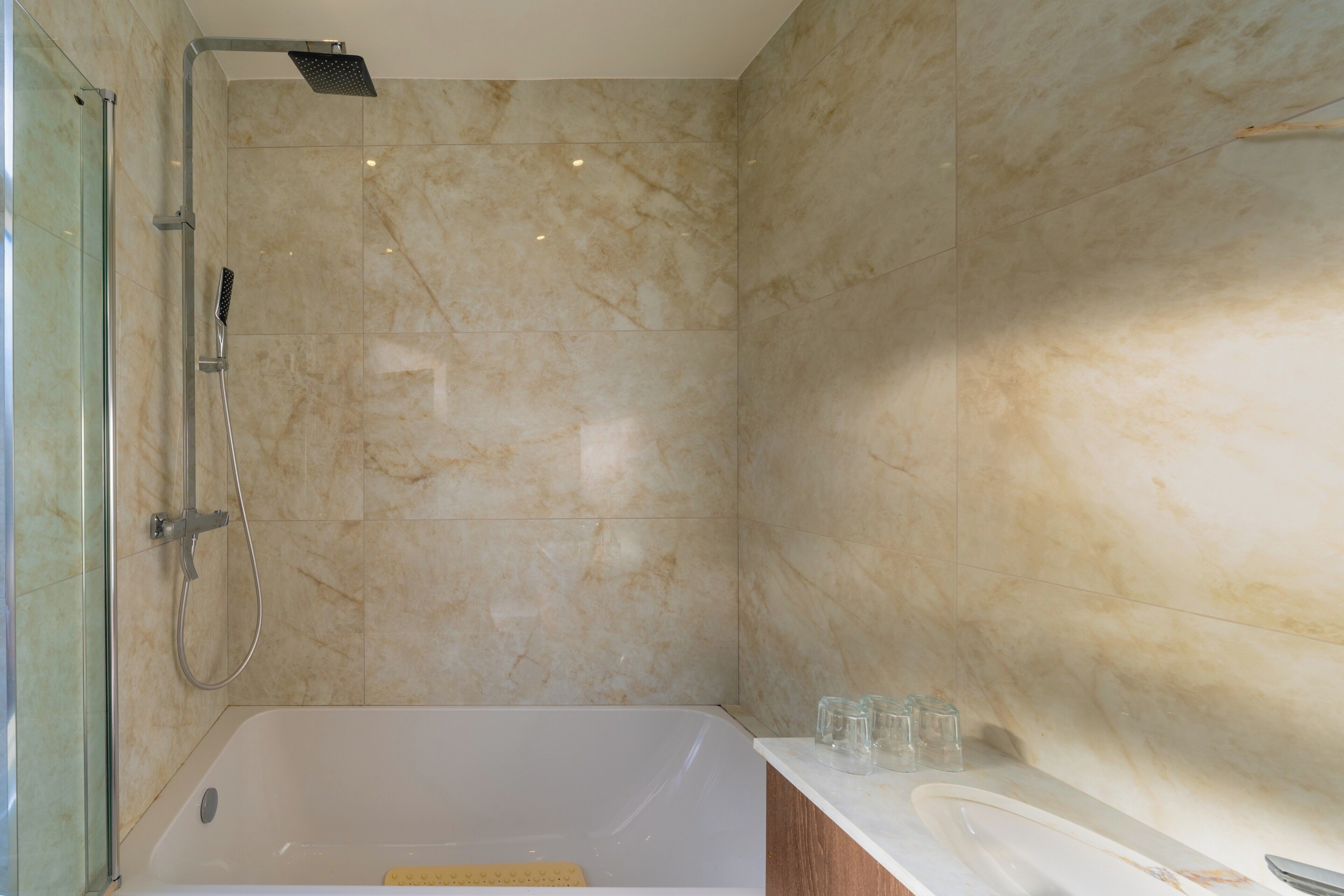 A modern bathroom with a bathtub, shower, and marble walls.