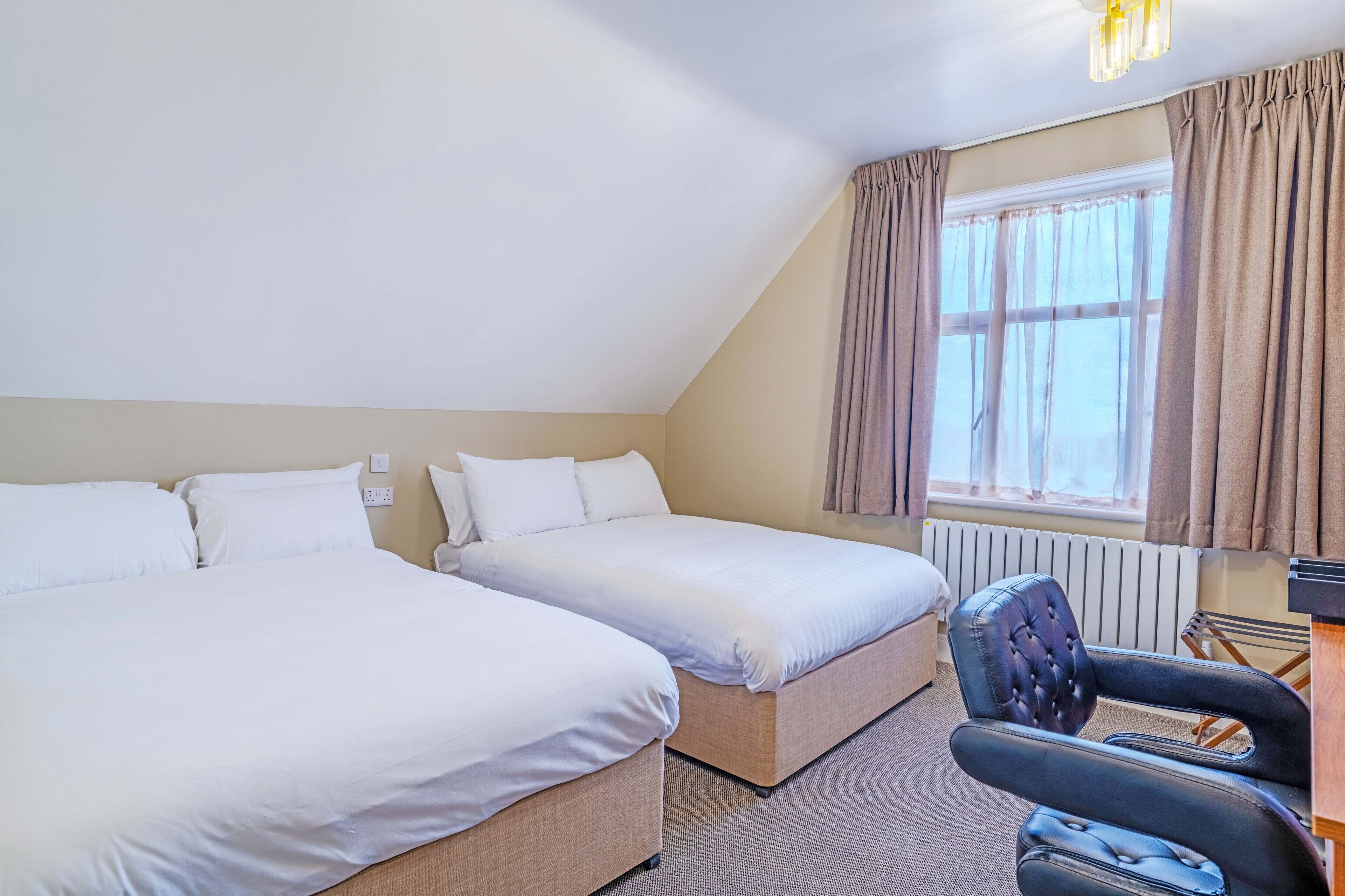 Hotellihuone, jossa on kaksi sänkyä, työpöytä, tuoli ja ikkuna, jossa on verhot.