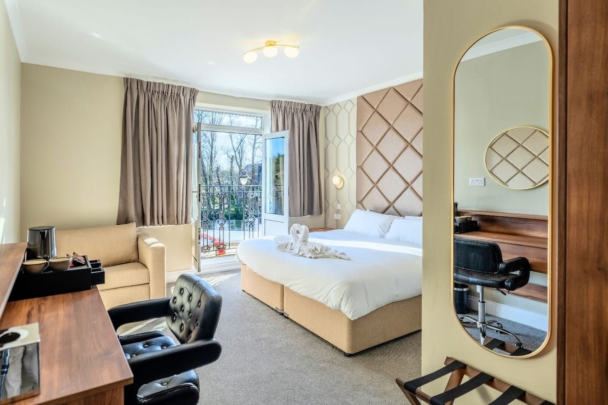 A hotel room with a bed, a desk with a chair, a large mirror, and a view of the outdoors.