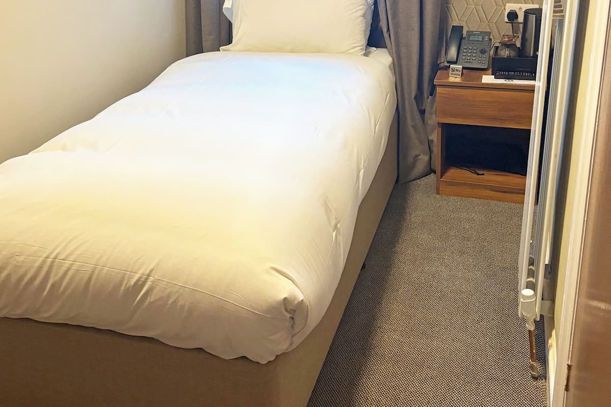 A hotel room with a bed, a nightstand with a phone, a lamp, and a window with curtains.