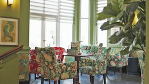 A room with floral patterned chairs, a round table, and a staircase with green walls and a framed picture. - Uno Thames Hotel (Maidenhead)