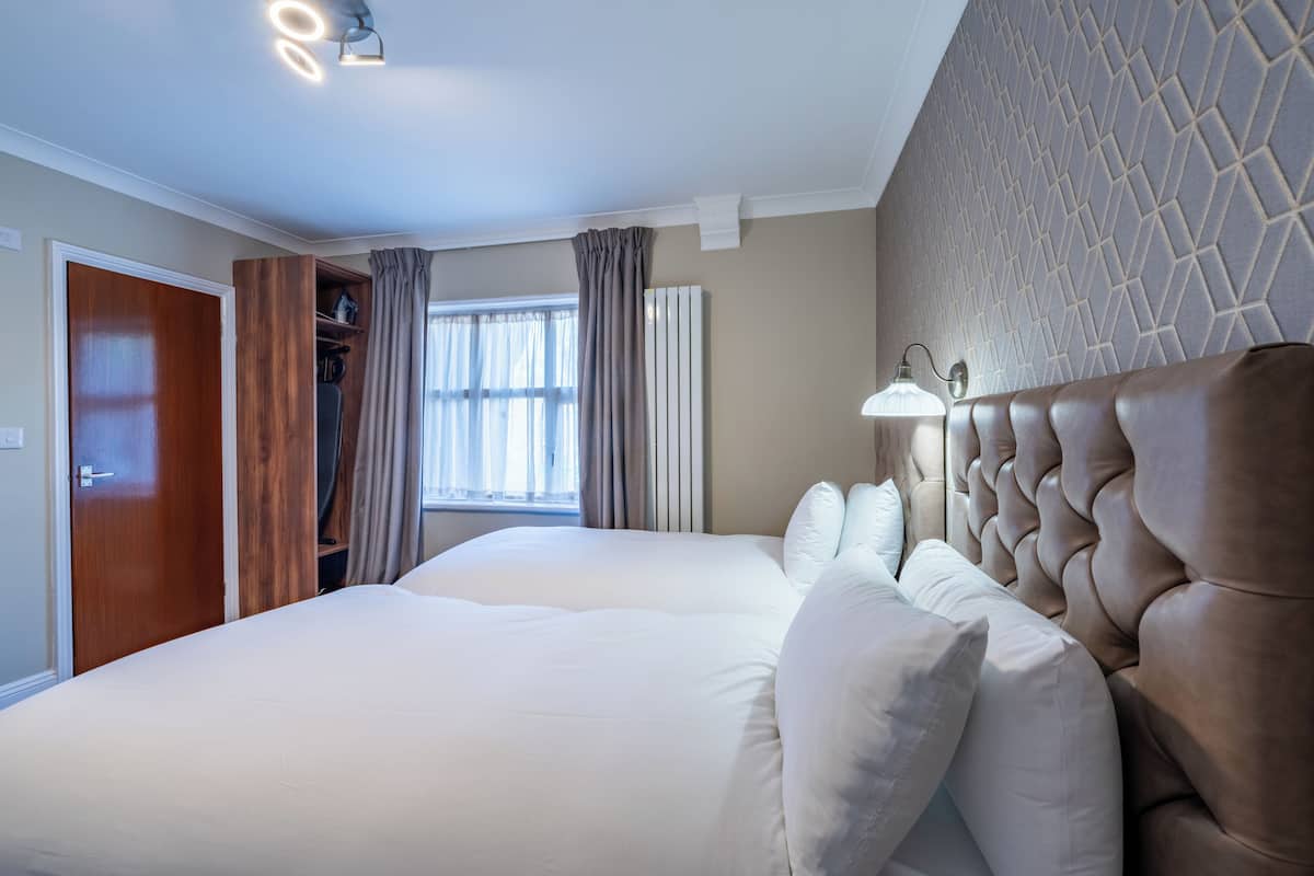 A hotel room with a large bed, a wardrobe, a window with curtains, and a wall with a geometric pattern.