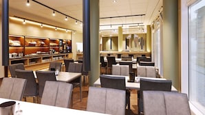 Un restaurante moderno con mesas y sillas altas, una zona de bar y un ventanal grande.