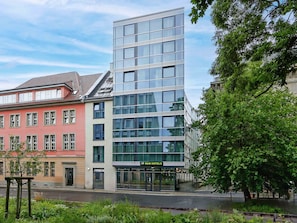 A modern hotel with a glass facade, a red building adjacent, and a tree-lined street. - B&B HOTEL Berlin-Mitte (Berlin)