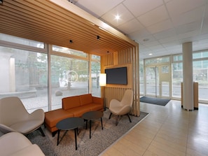 A modern waiting area with a wooden slatted ceiling, a sofa, two armchairs, a TV, and large windows offering a view of the outdoors. - B&B HOTEL Berlin-Mitte (Berlin)