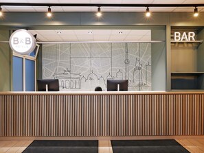 A reception desk with a B&B sign, a map wall, and a bar area. - B&B HOTEL Berlin-Mitte (Berlin)