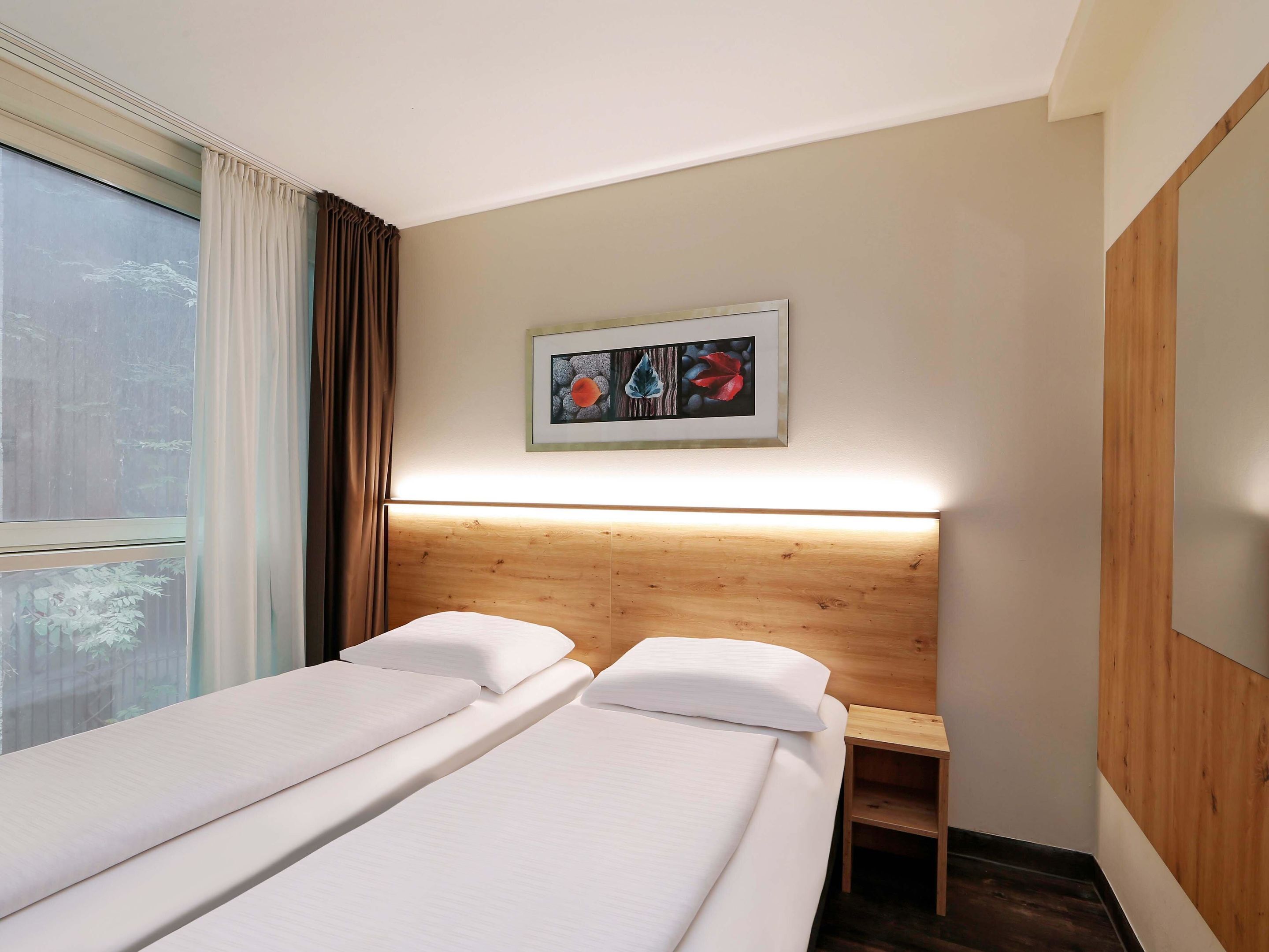 A hotel room with two single beds, a wooden headboard, a bedside table, and a framed picture on the wall.