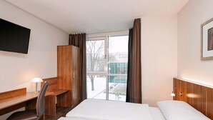 Habitación de hotel con cama, escritorio, silla, televisión y ventana con cortinas.