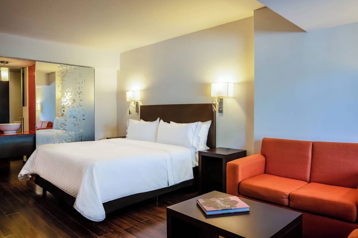 Ein Hotelzimmer mit einem Bett, einem Nachttisch, einer roten Couch und einem Tisch mit einem Buch.